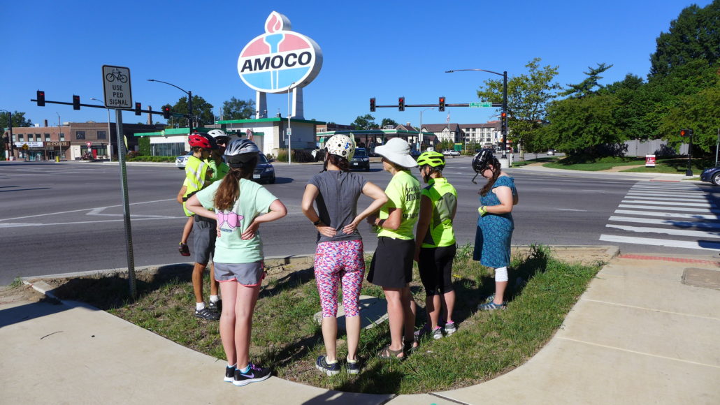 5 women stand next to a man holding a boy on street corner Amoco sign in background