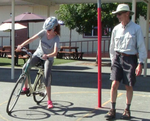 Adult student learning how to "power pedal" her bicycle as instructor looks on